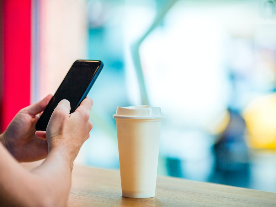 Closeup of male hands holding cellphone and glass of coffee in cafe