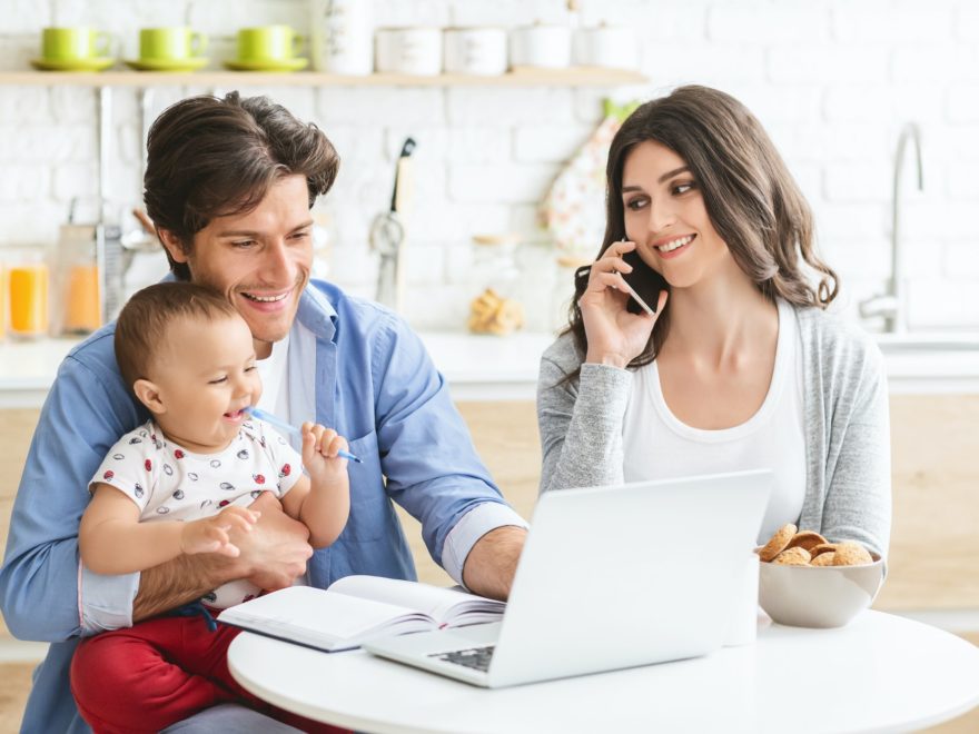 Millennial parents with baby son working on laptop at kitchen